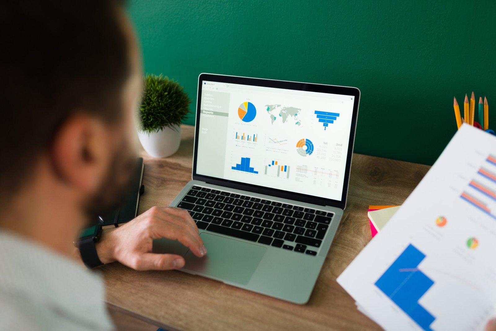 Rear view of a young man working on his laptop and looking at a work report and graphs